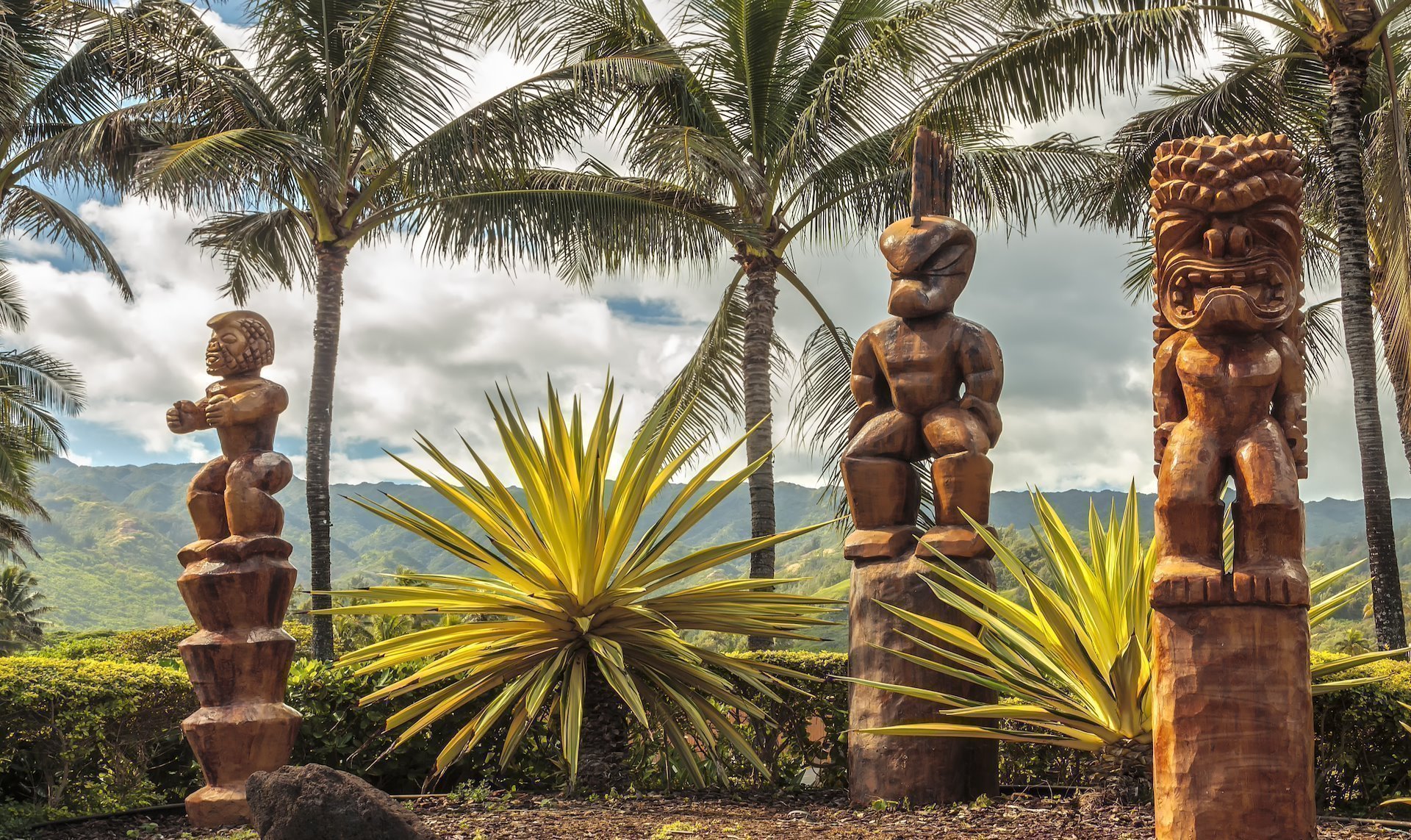 Three Polynesian tiki statues in a tropical background. Oahu, Hawaii